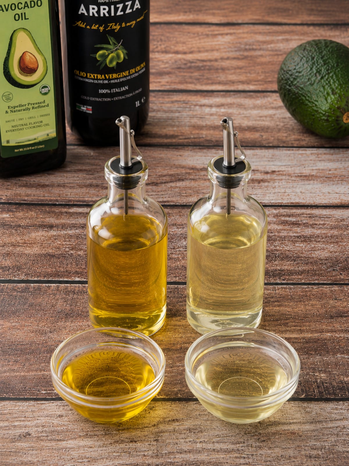 Side-by-side comparison of dark and light cooking oils in clear glass dispensers and bowls, illustrating the difference between cold-pressed and expeller-pressed oils.