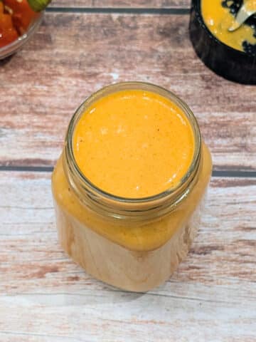 Creamy roasted red pepper Greek yogurt sauce in a glass jar.