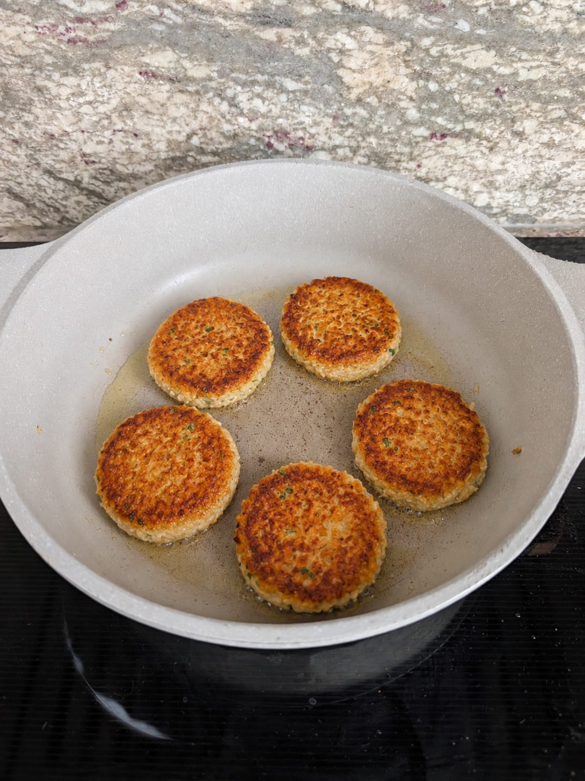 Golden Crispy Rice Fritters cooking on the second side in a skillet.