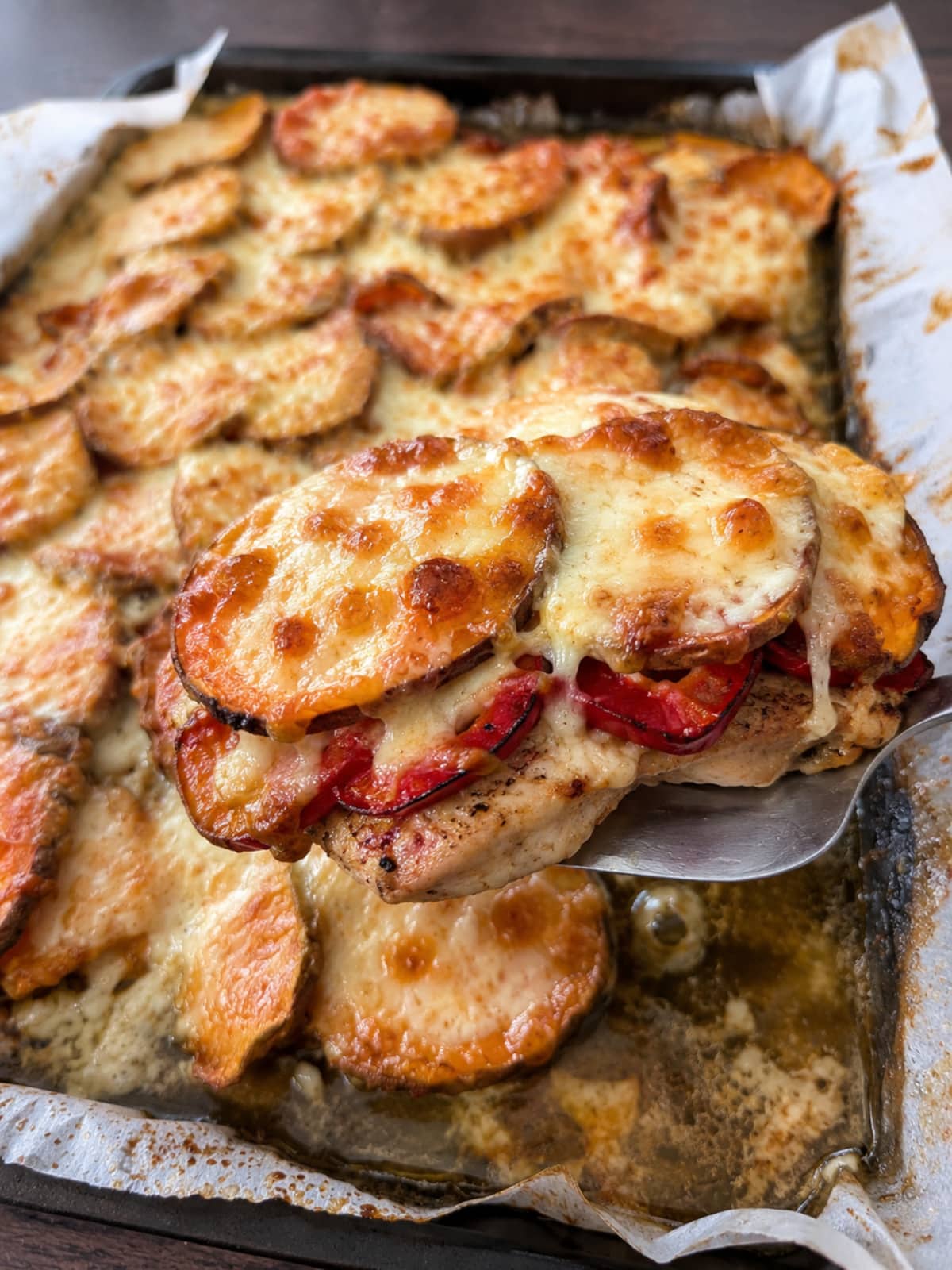Serving of baked chicken with roasted red peppers, sweet potatoes and melted mozzarella lifted from the sheet pan.