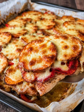 Serving of baked chicken with roasted red peppers, sweet potatoes and melted mozzarella lifted from the sheet pan.
