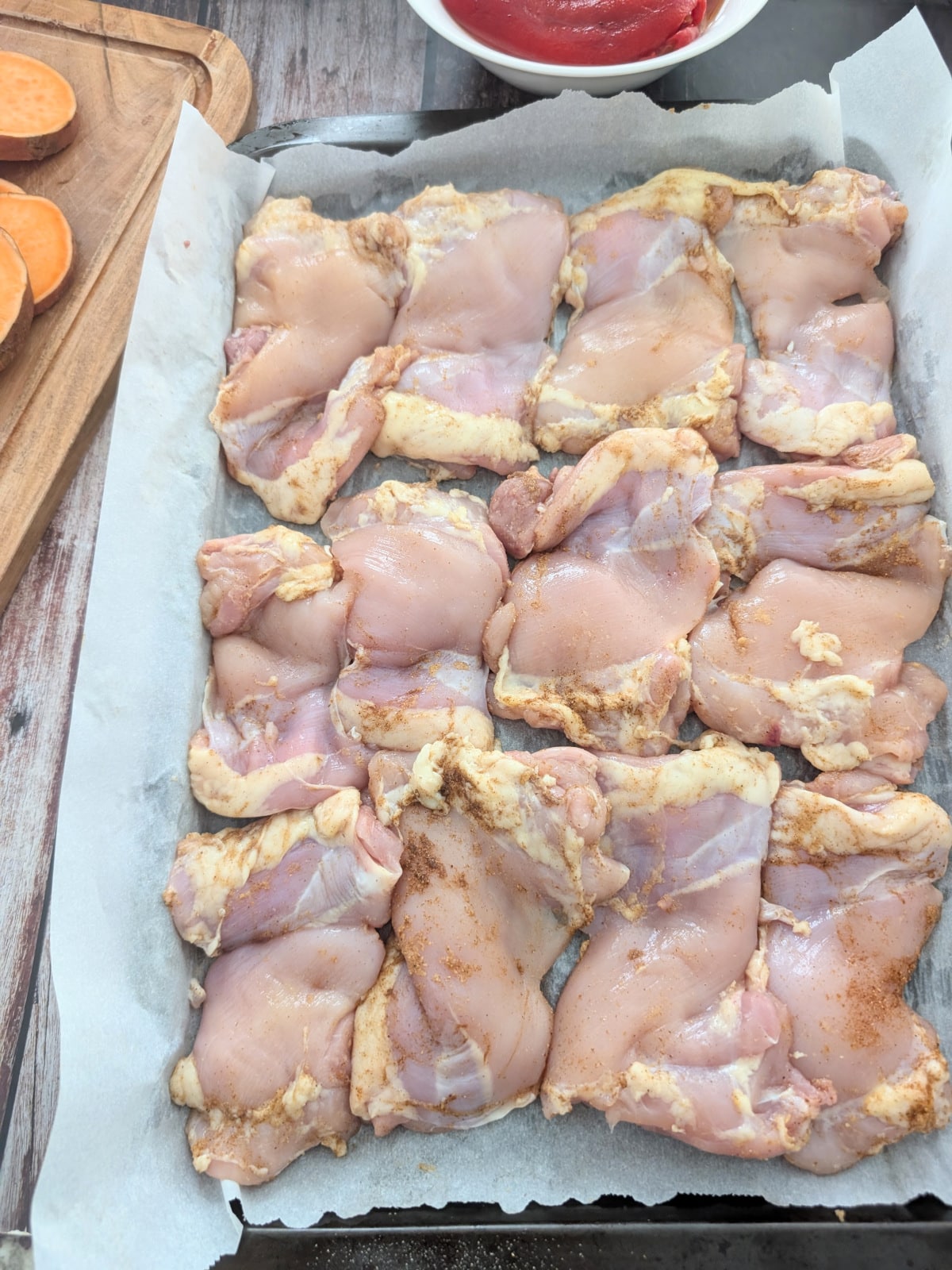 Boneless skinless chicken thighs seasoned with garam masala and garlic powder on a parchment-lined baking sheet.