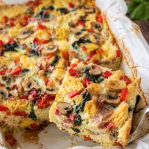 Easy breakfast strata with bread, eggs, ham, mushrooms, spinach, red peppers and melted cheese in a baking dish.