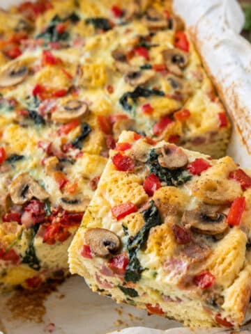 Easy breakfast strata with bread, eggs, ham, mushrooms, spinach, red peppers and melted cheese in a baking dish.