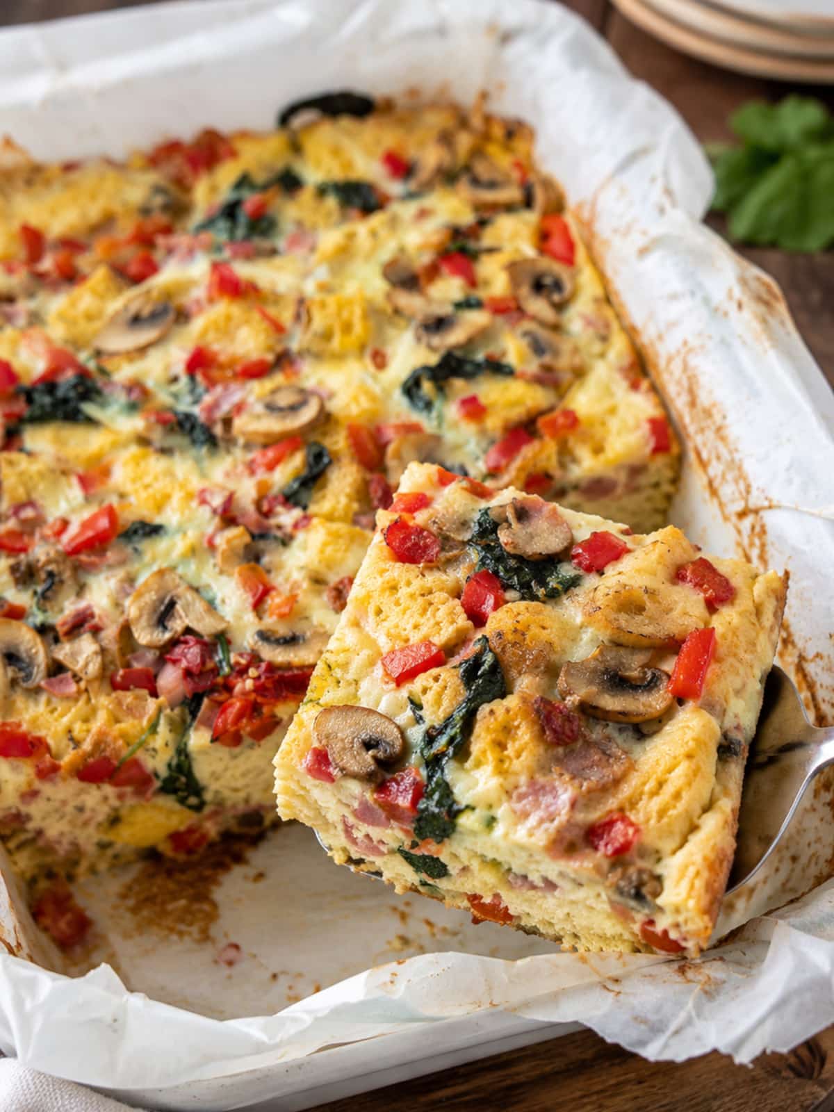Easy breakfast strata with bread, eggs, ham, mushrooms, spinach, red peppers and melted cheese in a baking dish.